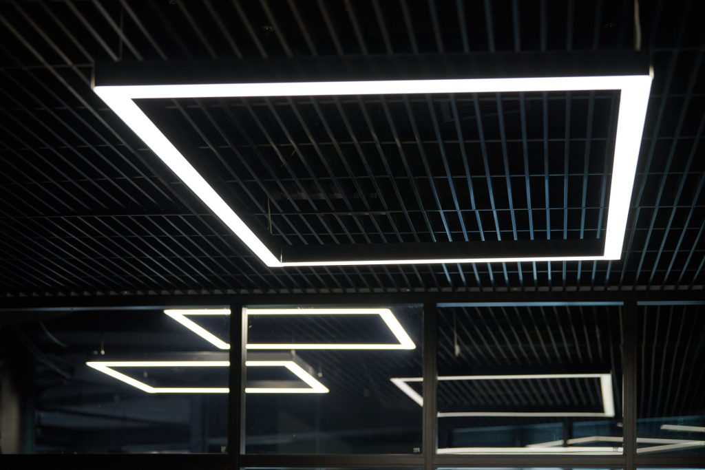 Modern office lighting. Thin lamps in office dark ceiling. LED white cold light over workplaces.
