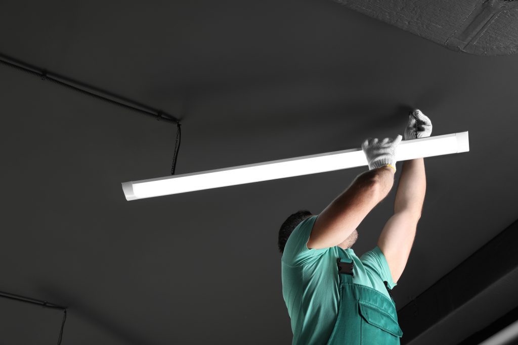 Ceiling light. Electrician installing led linear lamp indoors.